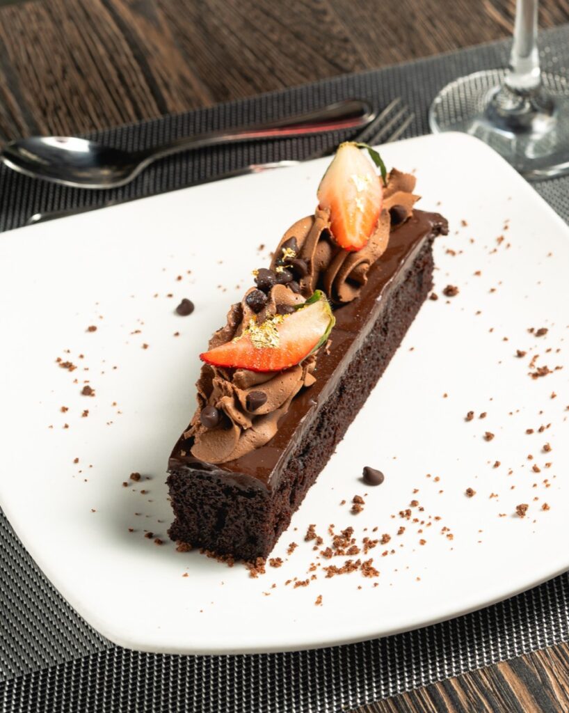 A slice of dark chocolate ganache cake with strawberry and chocolate curls